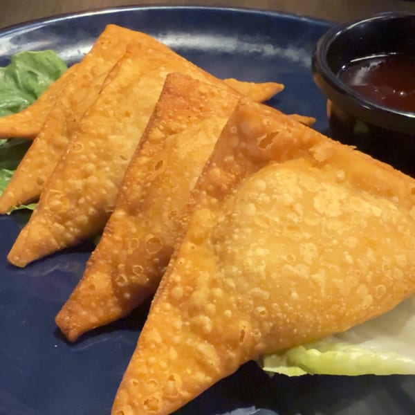 Golden-fried wontons from The Dragon Asian Kitchen, served on a blue plate with lettuce and dipping sauce.