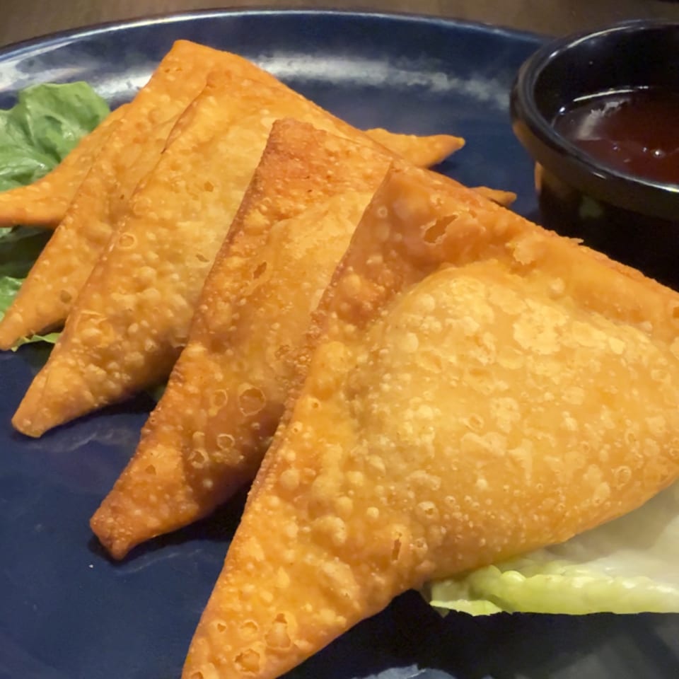 Golden-fried wontons from The Dragon Asian Kitchen, served on a blue plate with lettuce and dipping sauce.