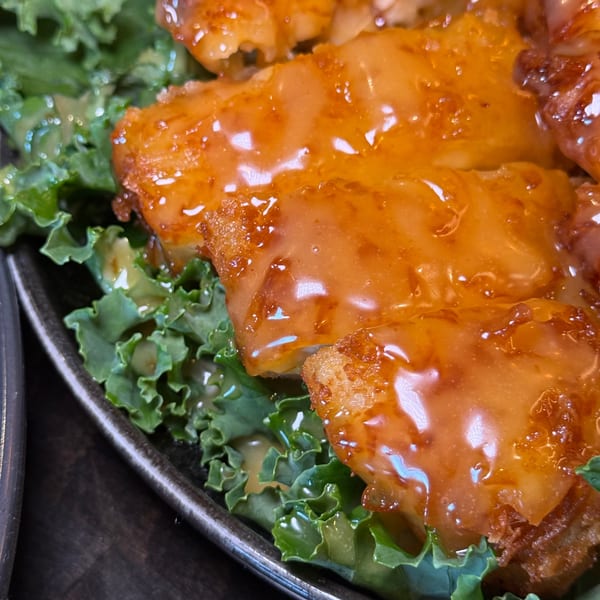 Close-up of crispy orange chicken with a glossy sauce, served on a bed of fresh green lettuce.